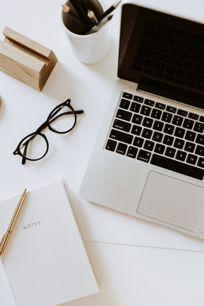 overhead shot of computer that is open, notepad with pen, glasses and coffee