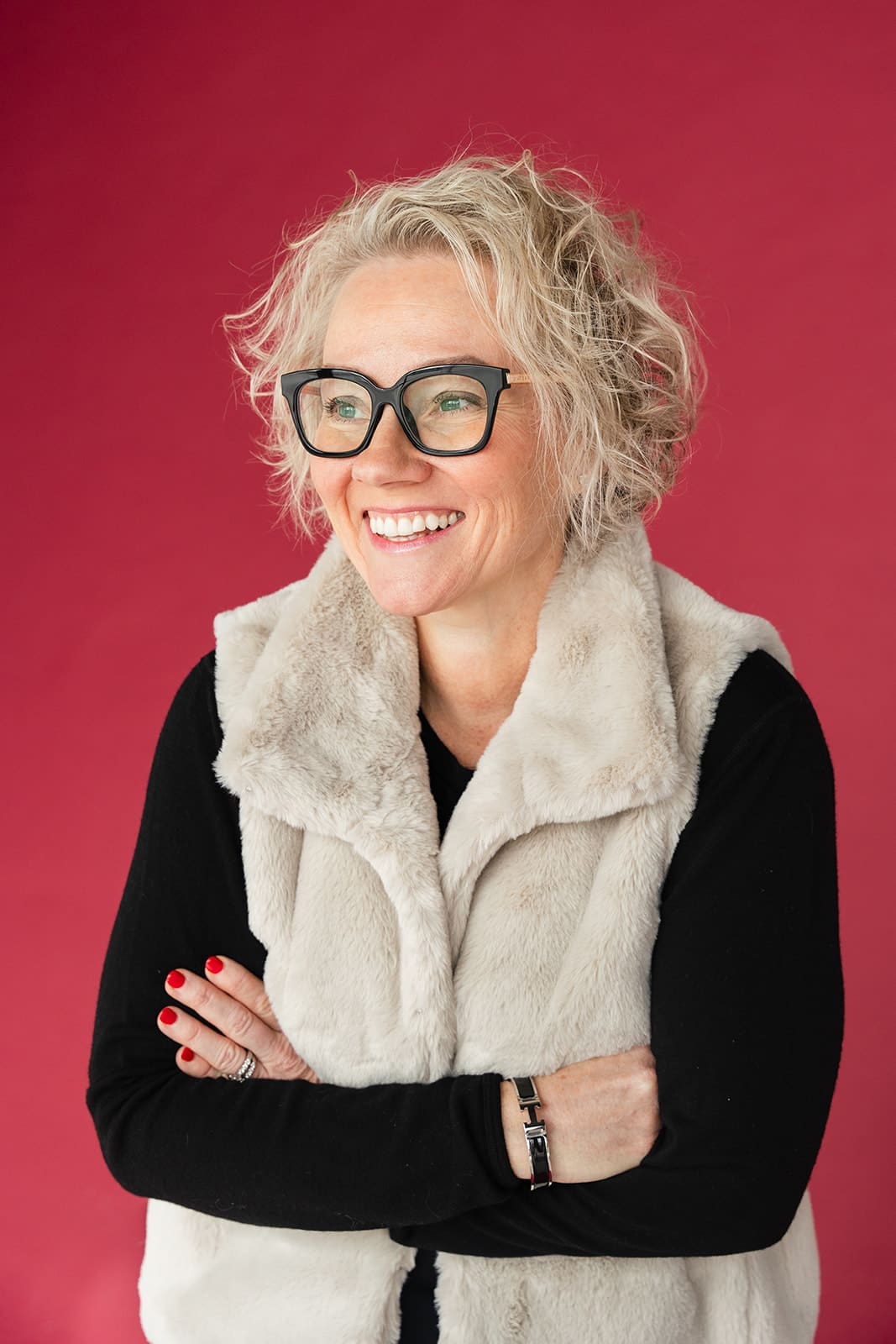 Cindy Gordon in glasses and a cream vest smiling against a deep red background