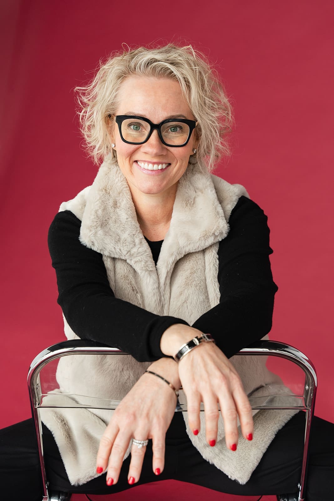 Cindy Gordon seated on a chair in a cream vest against a deep red background