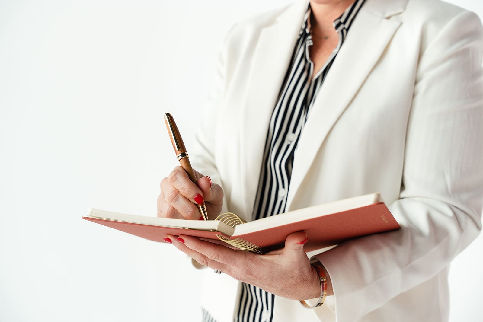 Cindy Gordon writing in a notebook in a cream blazer and striped top