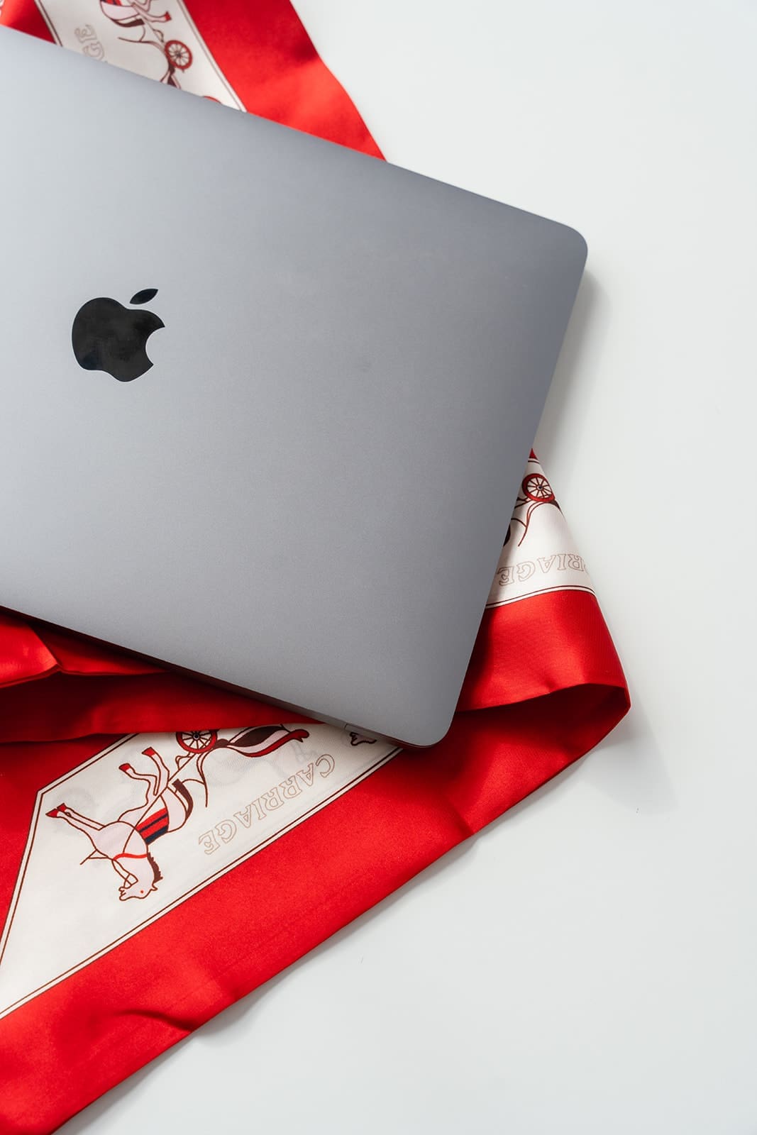 A closed silver laptop resting on a red patterned scarf