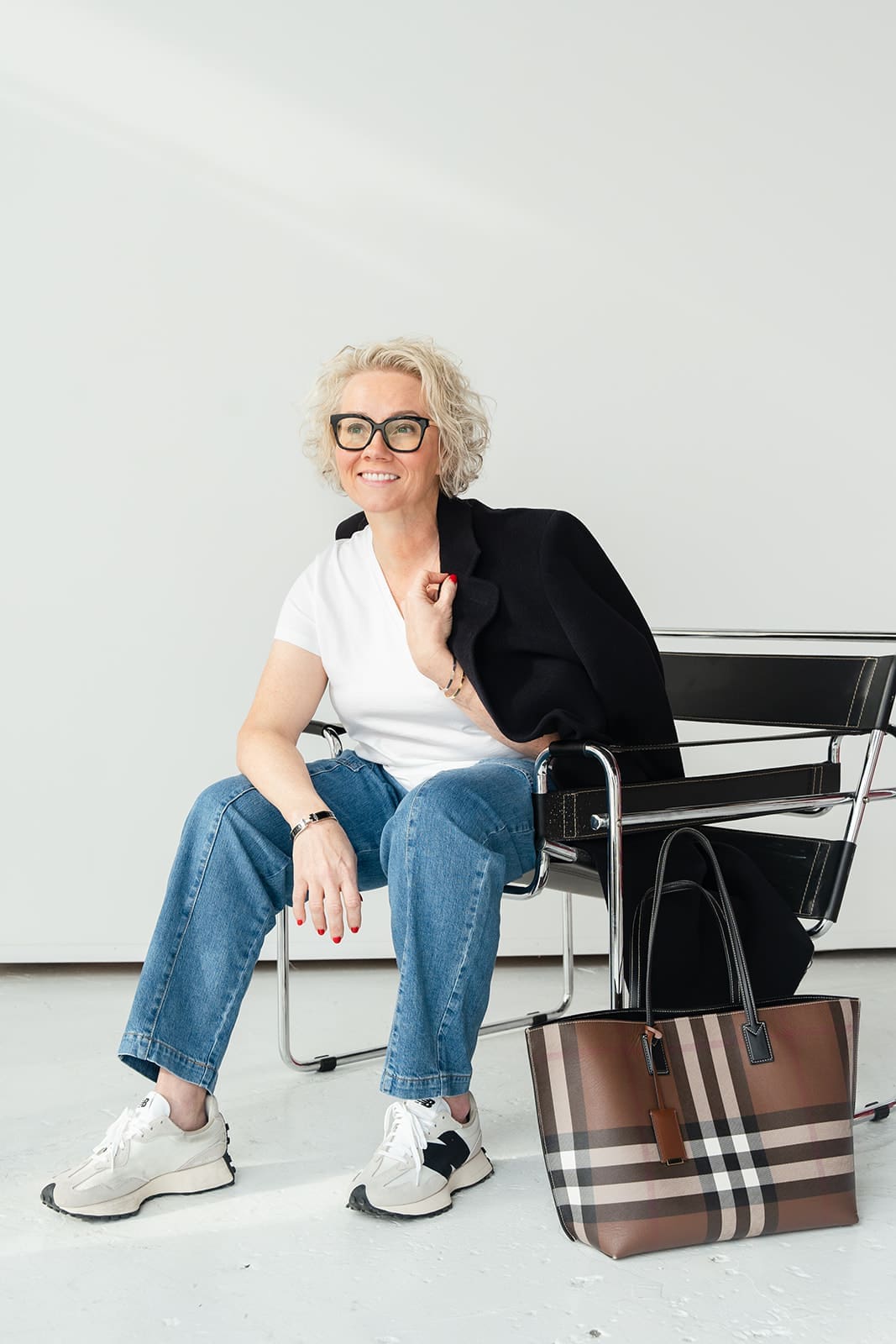 Cindy Gordon seated in jeans and a white top holding a mug, with a striped bag beside her