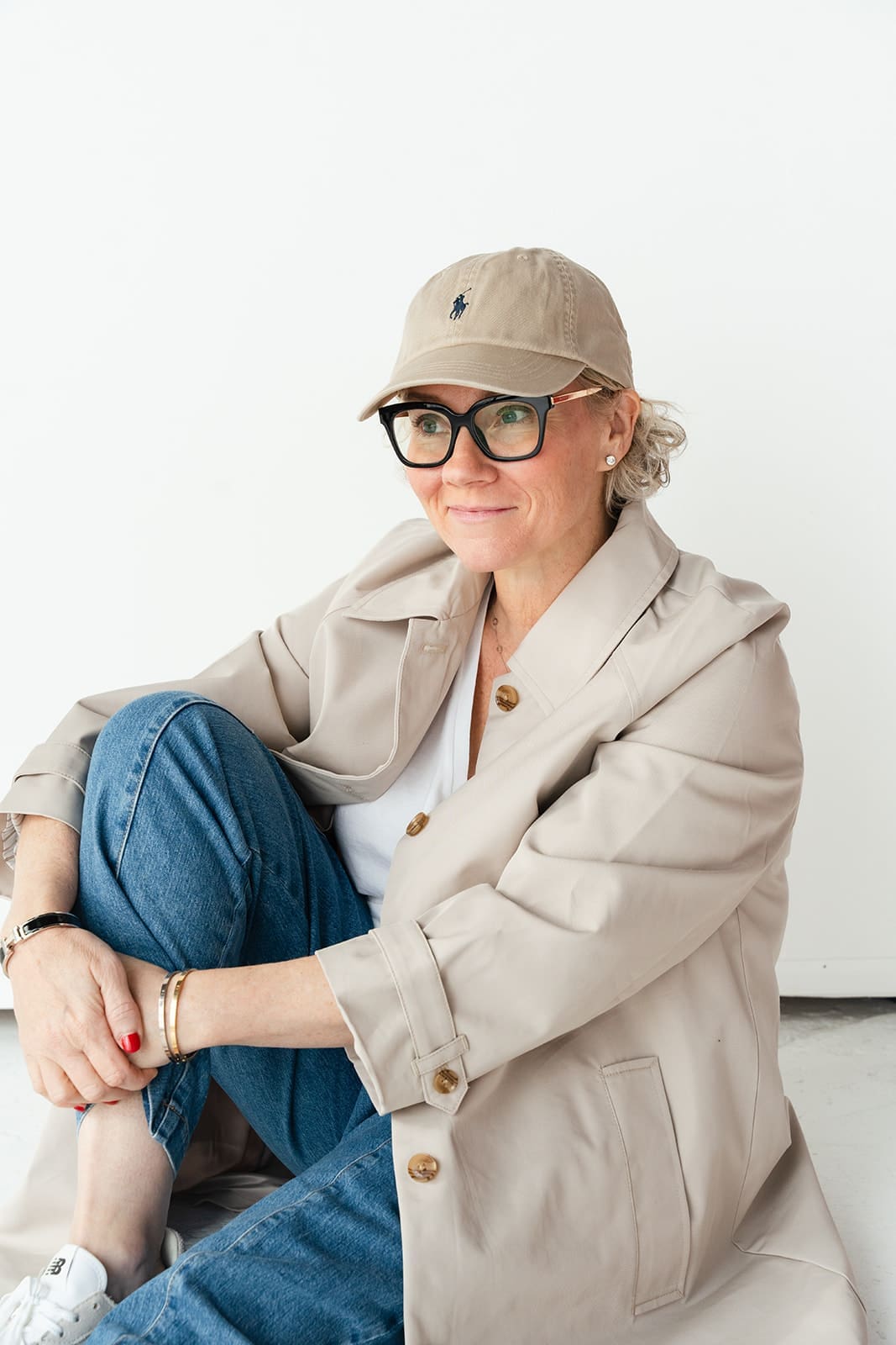 Cindy Gordon seated in a cream jacket, cap and jeans with her chin on her hand