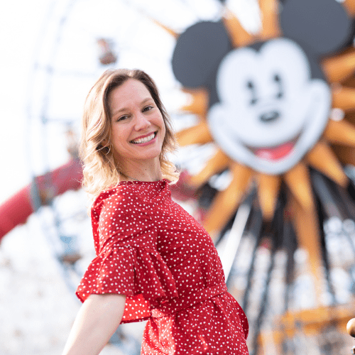 Kim Stuffed Suitcase in a red dress with a Mickey Mouse sign in the back ground of this travel agent photo